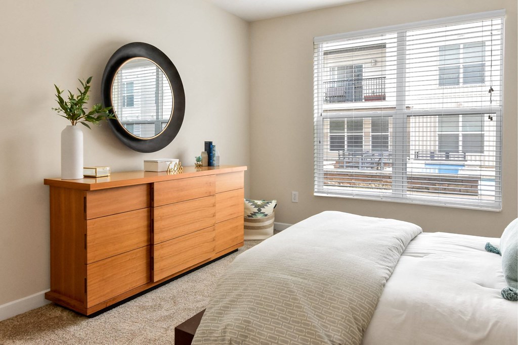 A bedroom with a large bed, a wooden dresser, and a round mirror on the wall.