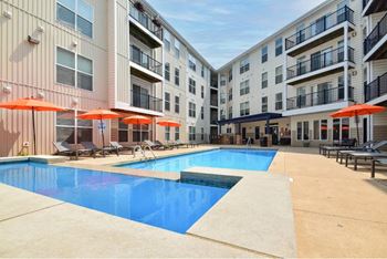 A swimming pool surrounded by apartment buildings and lounge chairs.