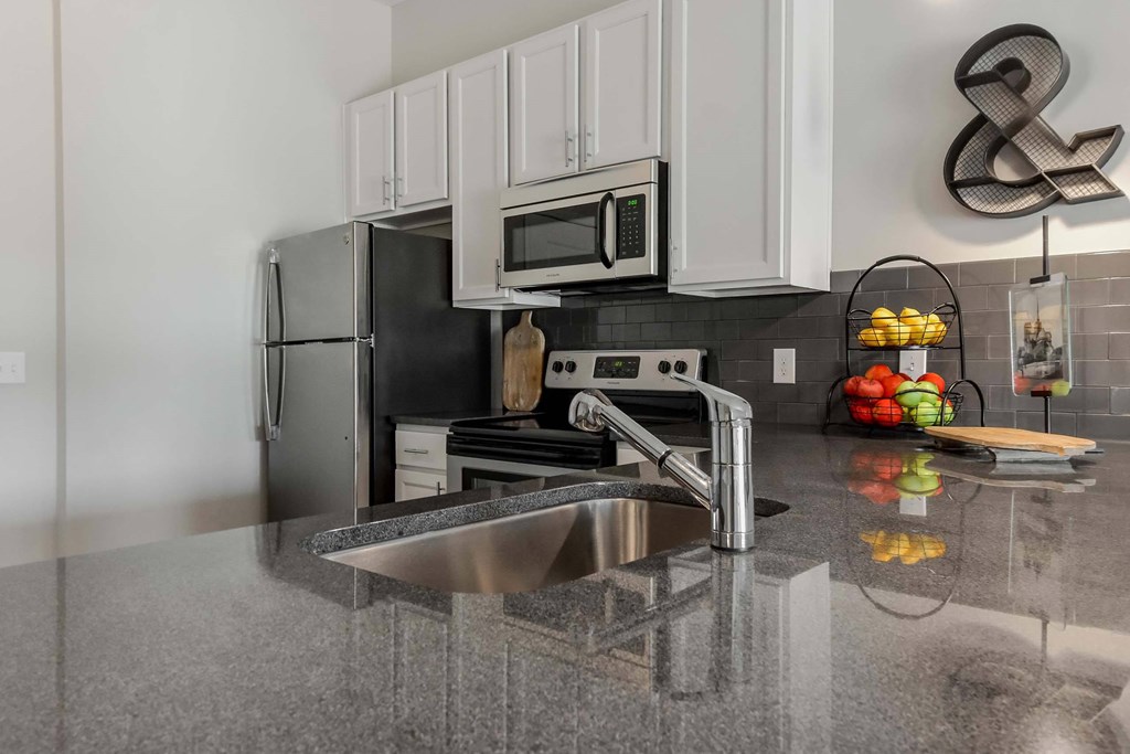 A modern kitchen with a black fridge and a black and white tiled backsplash.