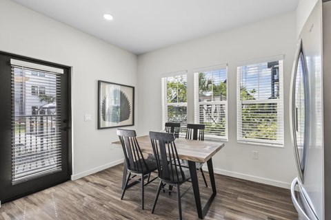A dining room with a table and chairs and a fridge.