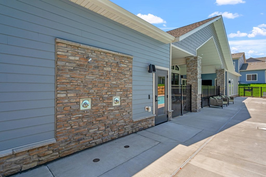 A building with a grey siding and a stone wall with two signs on it.