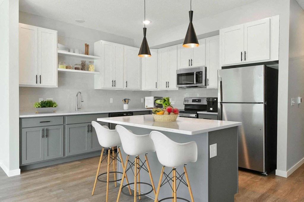 A modern kitchen with a large island and white chairs.