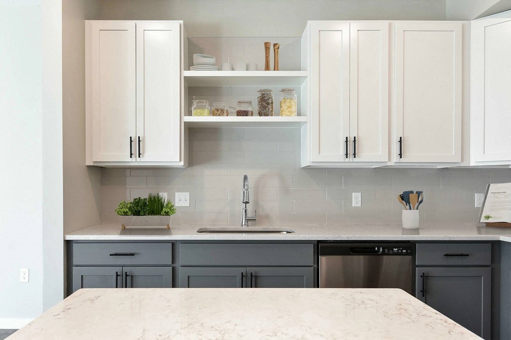 A kitchen with a marble countertop and grey cabinets.