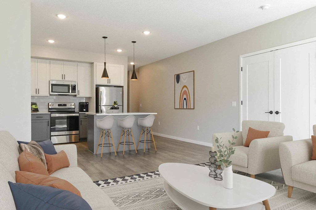 A modern kitchen with a breakfast bar and a living room with a couch and chairs.