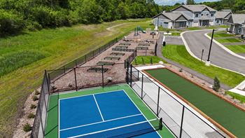 A tennis court surrounded by a fence with a residential area in the background.