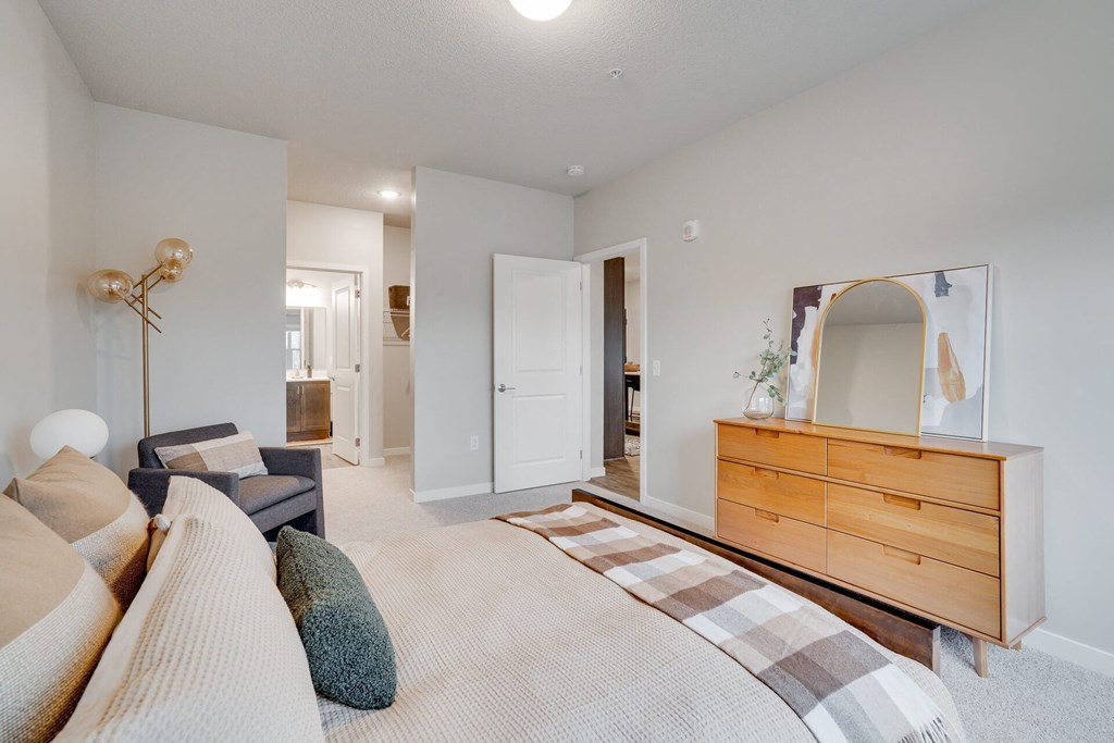 A well-lit bedroom with a large bed and a dresser with a mirror.