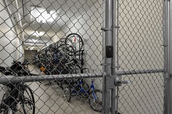 A chain link fence with a gate is in front of a wall with a bunch of bicycles hanging on it.