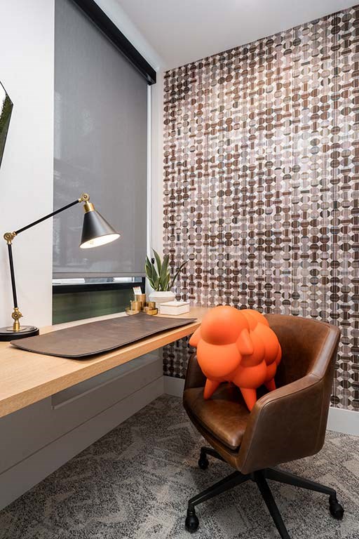 A chair with an orange design on it sits in front of a desk with a lamp on it.