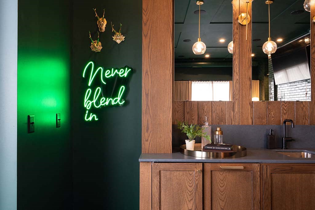 A kitchen with a green neon sign that says "Never blend in".