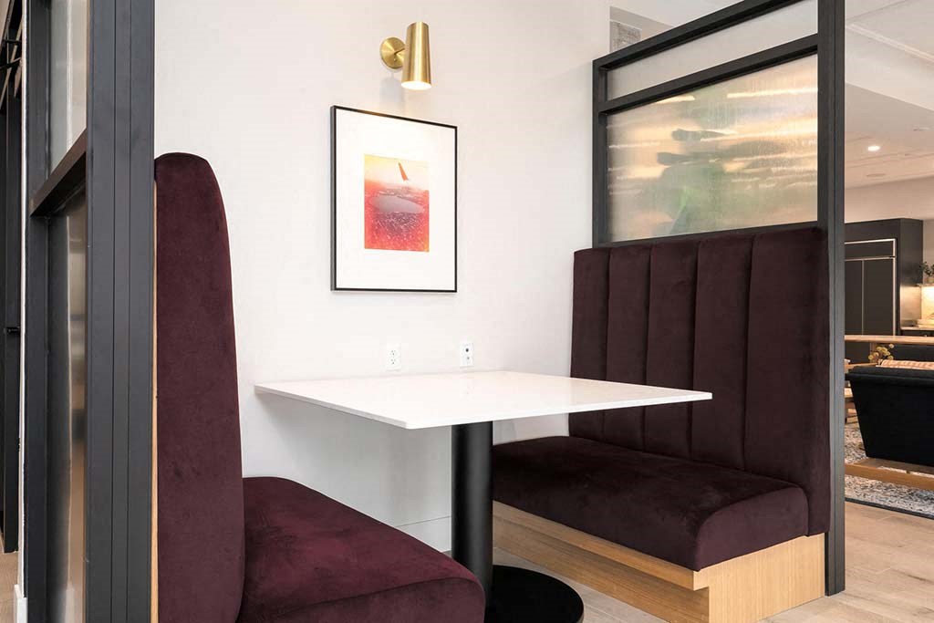 A white table with a red chair and a framed picture of a drink on the wall.