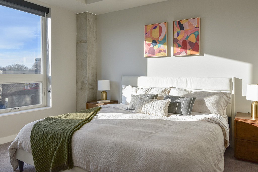 A bedroom with a large bed and two abstract paintings on the wall.