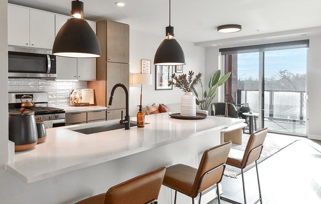A modern kitchen with a white countertop and brown chairs.