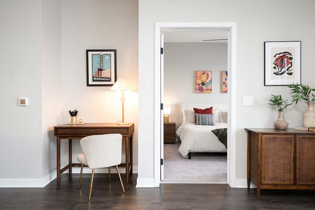 A room with a desk and a bed in the background.