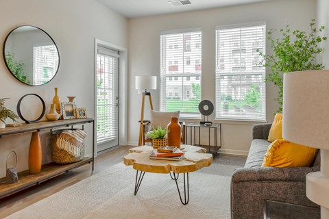 A living room with a grey couch, a round mirror, and a table with a plant on it.