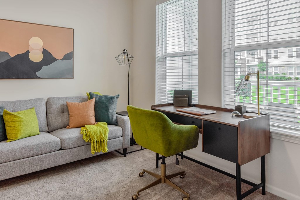 A room with a grey couch, a green chair, and a desk with a laptop on it.