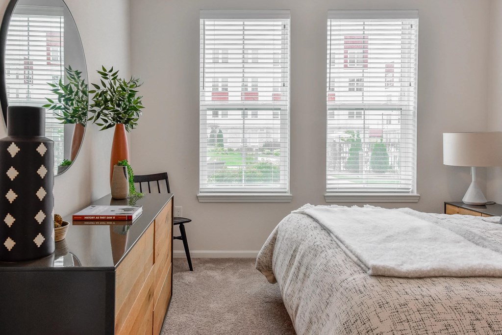 A bedroom with a bed, a dresser, and a window with blinds.