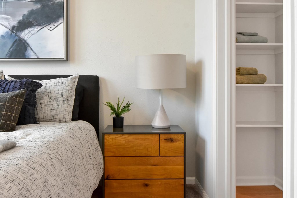 A bedroom with a bed, a nightstand with a lamp, and a shelf with towels.