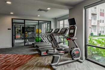 A gym with treadmills and a view of a building outside the window.