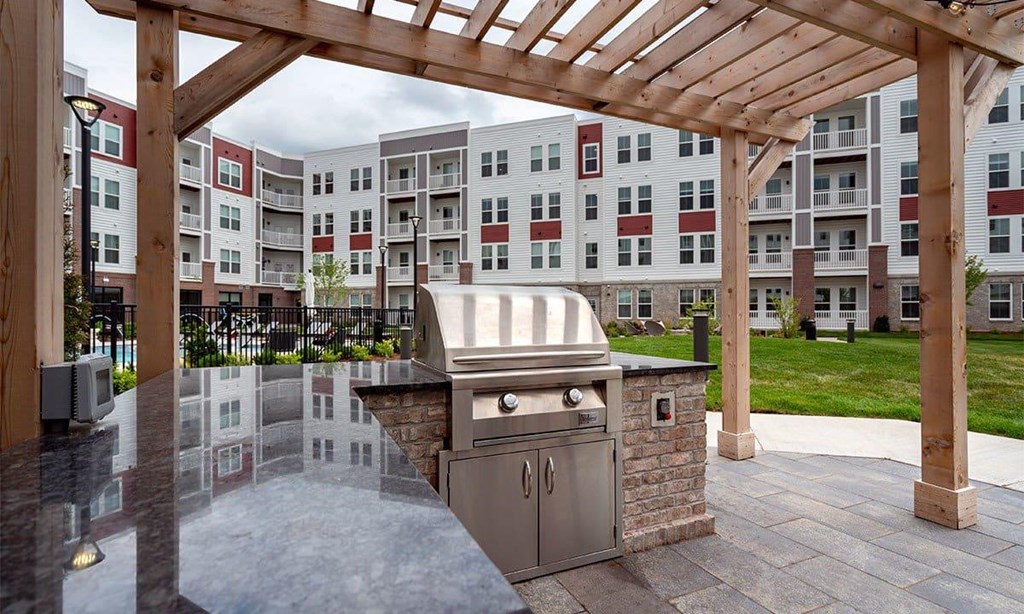 A BBQ grill is situated under a wooden pergola in a courtyard.