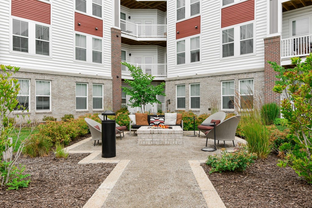 A courtyard with a black trash can and a bench with a cushion on it.