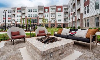 A fire pit sits in the middle of a patio with two chairs and a couch.