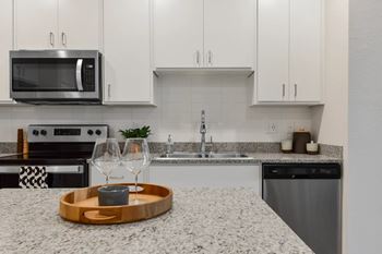 A modern kitchen with a granite countertop and a wooden tray with a candle on it.