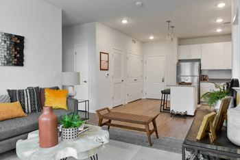 A living room with a grey couch, a coffee table, and a kitchen area in the background.