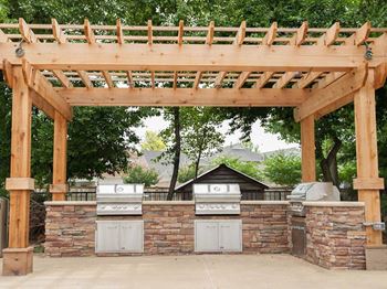A wooden pergola over a stone wall with two grills.
