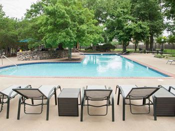 A pool surrounded by trees and chairs.