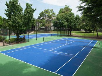 A blue tennis court surrounded by green trees.
