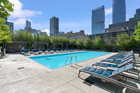 A swimming pool with lounge chairs and a city skyline in the background.