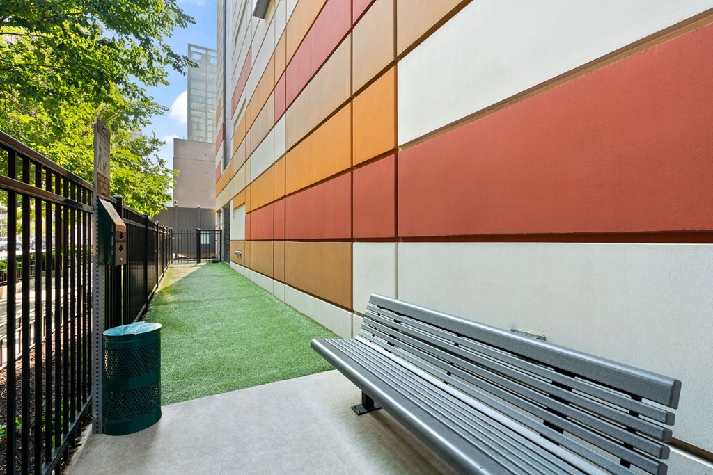 A bench is on a sidewalk next to a green trash can.