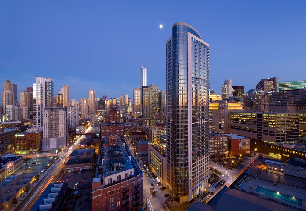 A cityscape at dusk with a moon visible in the sky.