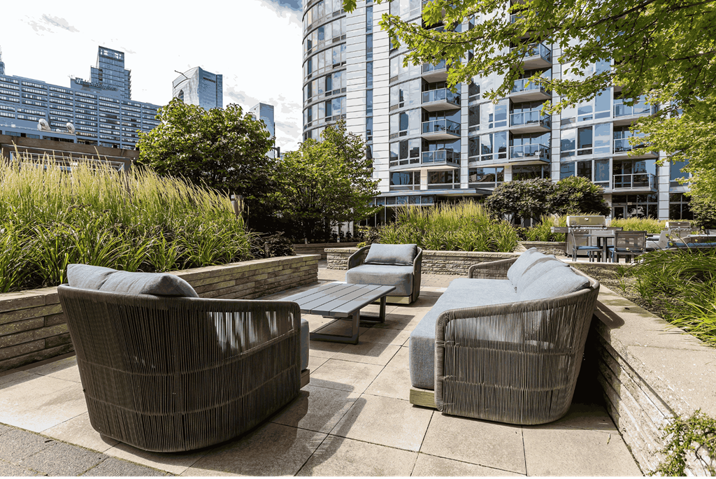 A patio with wicker chairs and a table with a view of a city skyline.