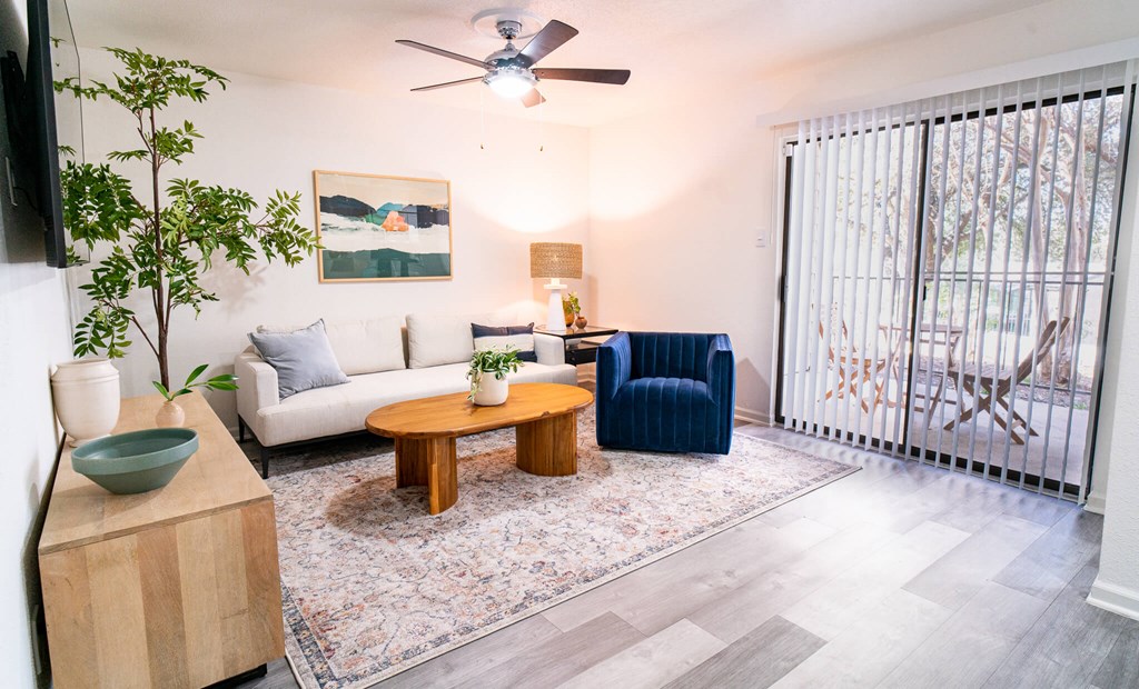 A living room with a white couch, a blue armchair, a wooden coffee table, and a flat-screen TV mounted on the wall.