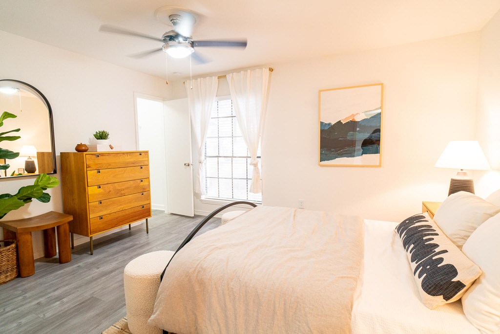 A bedroom with a large bed, a wooden dresser, and a painting on the wall.