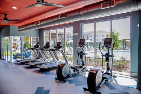 A gym with a row of stationary bikes and a ceiling fan.