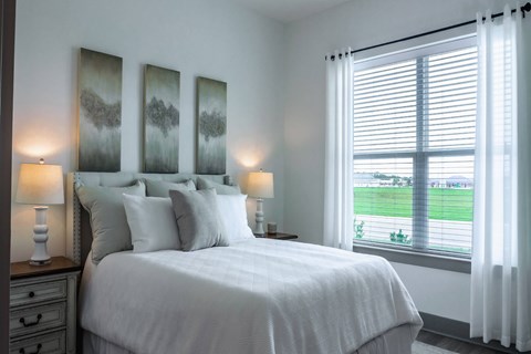 A bedroom with a large bed, two lamps, and a window with a view of a green field.
