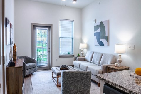 A living room with a grey couch, a grey chair, a wooden table, a lamp, and a painting on the wall.
