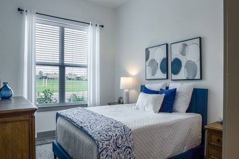A bedroom with a large bed and a window overlooking a green field.