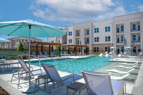 A pool area with chairs and umbrellas in front of a building.