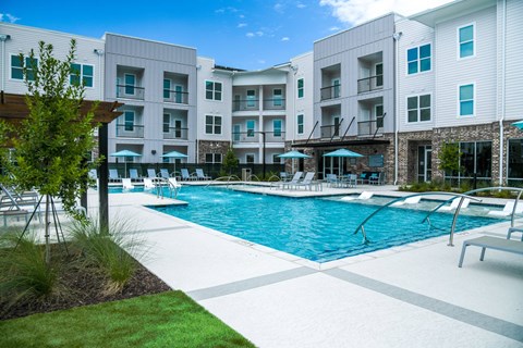 A swimming pool surrounded by a grassy area and a building in the background.