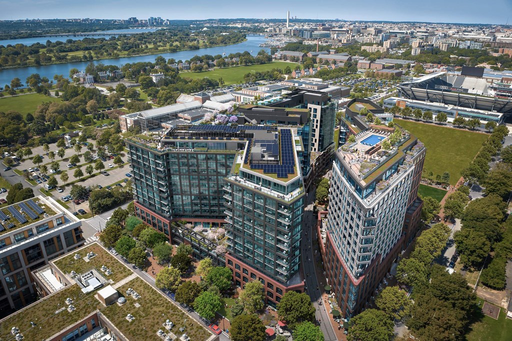 A modern building complex with a green roof is surrounded by trees and other buildings.