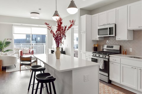 A kitchen with white cabinets and a white island with a vase of red flowers on top.
