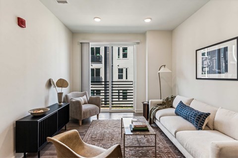 A living room with a white couch, a brown chair, a black piano, and a window with blinds.
