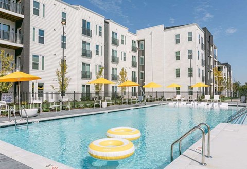 A swimming pool with yellow umbrellas and floating yellow chairs in front of a white building.