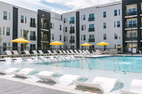 A pool area with sun loungers and umbrellas in front of a white building.