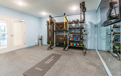 A room with a yoga mat on the floor and a rack of exercise balls.