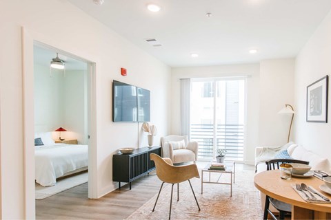 A well-lit, modern bedroom with a large bed, a chair, a table, and a television.