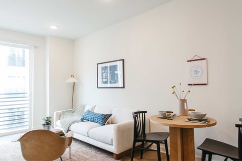 A living room with a white couch, a wooden table, and a brown chair.